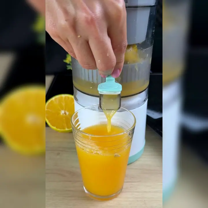 Zumo de naranja saliendo por la palanca verde agua del exprimidor hacia un vaso de cristal